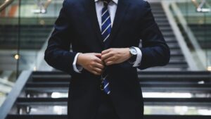 Man's torso in a suit, buttoning his coat and wearing a wrist watch descending stairs