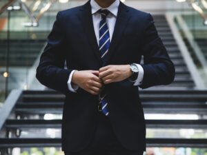 Man's torso in a suit, buttoning his coat and wearing a wrist watch descending stairs